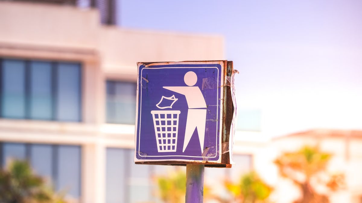 Close-up of a recycling sign against a modern building backdrop in a sunny urban setting.